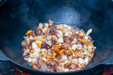 The process of cooking Asian pilaf on fire. Meat is fried in a cauldron, close-up.