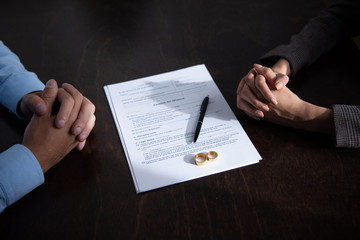 partial view of couple sitting at table with clenched hands near divorce documents and rings