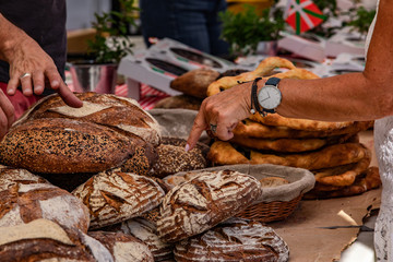 Baked goods at outdoor agriculture fair. A market trader and are shopper are seen closeup by a baker's stand with rustic loaves of bread as person purchases locally produced food.