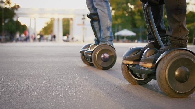 Close up shot of two elegant businessmen riding hoverboard in city park on sunny day, slow motion