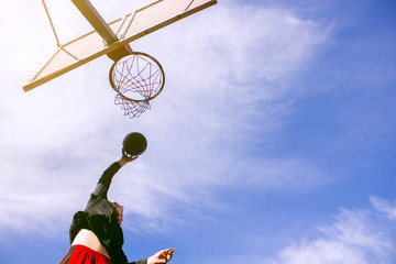 Bottom view of a young athlete performing a dunk in a jump. View of a basketball hoop in bright...