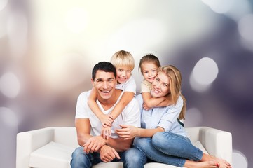 Loving parents with their little son and daughter posing together for a portrait leaning over the back of a large sofa in the living room