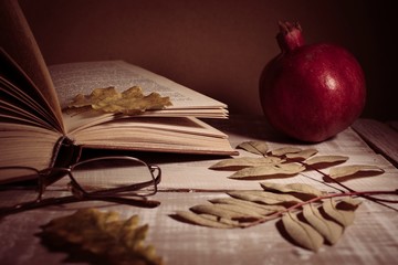Open book, glasses, pomegranate and autumn leaves on a wooden table. Autumn still life.