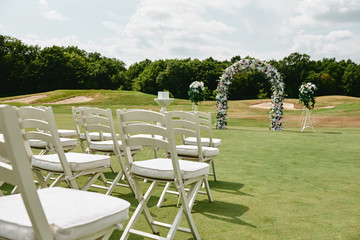 White wooden chairs on each side of archway outdoors, copy space. Empty chairs for guests prepared for wedding ceremony