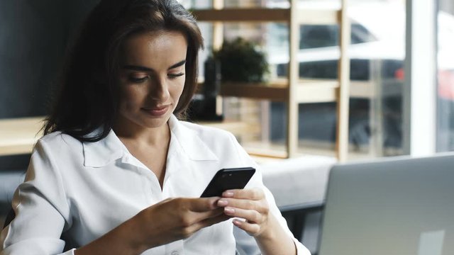 young woman in white formal shirt using her phone in cafe