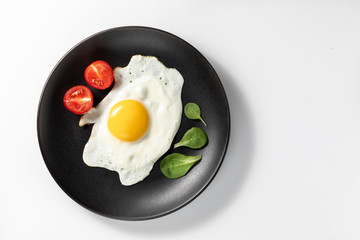 Fried eggs with fresh lettuce and tomatoes on a black plate. Isolated on white background.