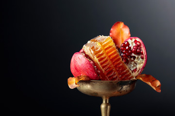 Ripe pomegranate fruits with honey in old brass vase.