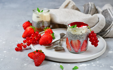 strawberry chia seeds dessert (chia pudding) with yogurt, red currants and jam. recipe healthy dessert in a round jar on a white plate, gray background