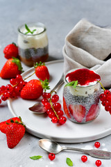 strawberry chia seeds dessert (chia pudding) with yogurt, red currants and jam. recipe healthy dessert in a round jar on a white plate, gray background