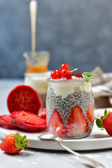 strawberry chia seeds dessert (chia pudding) with yogurt, red currants and jam. recipe healthy dessert in a round jar on a white plate, gray background