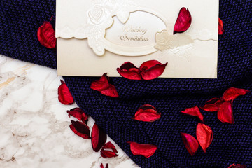 wedding card invitation above winter blue scarf and decorated with red dried flowers 