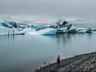 Woman in red jacket walking alone on the beach near iceburgs at Jokulson Lagoon, Iceland