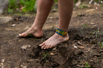 Diverse people enjoy spiritual gathering A closeup view of a barefooted woman wearing a colorful beaded ankle bracelet and standing on muddy soil, close to nature, during a retreat for body and mind.