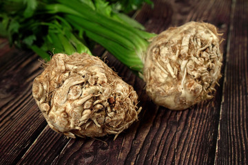 Fototapeta premium Celeriac / turnip-rooted celery roots with green leaves on dark wooden board, closeup detail