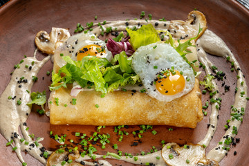 Rolled pancakes on top lies scrambled eggs. Beautiful clay plate.