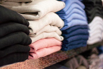 Warm clothing neatly folded on a store shelf. Sweatshirts, sweaters, jumpers, cardigans, hoodies, bobmers with piles on the shelf. Clothes storage. Size range.