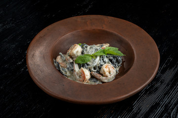 Black spaghetti with prawns on a black wooden table.