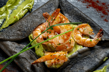 Pancakes made of black dough, with shrimp and sauces. Laid out on black slate. Wasabi and red pepper.