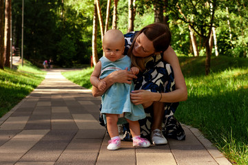 Mom teaches daughter to walk. Happy mom and daughter. Mom with a one-year-old daughter in dresses are walking in the park. Teaching children, motherhood. The first steps.