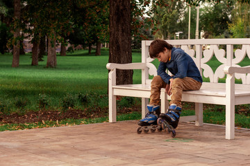 A teenager in roller skates is sitting on a bench in a park. Healthy lifestyle. Sports kids.