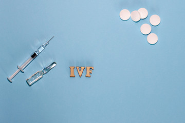 The abbreviation IVF is laid out in wooden letters on a blue background. In vitro injection pen,...