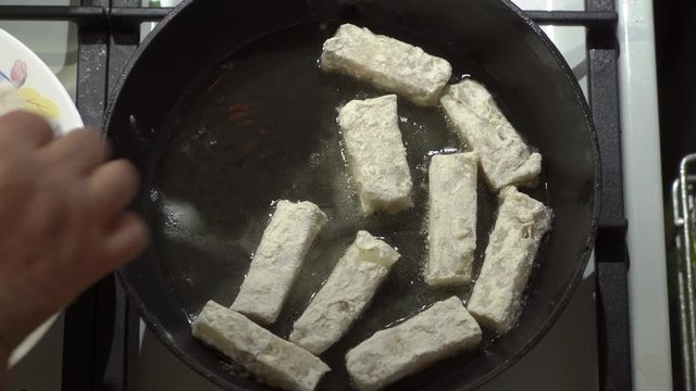 Making pan fried cod fish fillet in cast iron frying pan with cooking oil on gas stove.