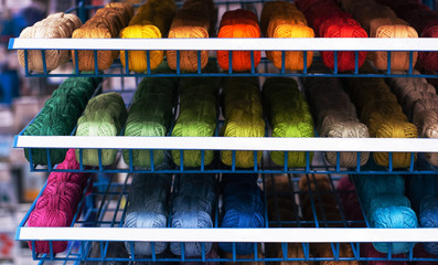 Shelf in a store with multi-colored skeins of yarn. Woolen, acrylic, silk thread. Knitting and crocheting. Preparing for the fall - knitting warm clothes. Needlework, hand made