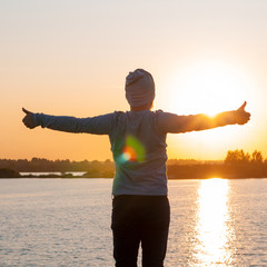 Vertical photo. A young man, a hipster, stands on a lake at sunset, enjoys the view while traveling, desolation, enjoyment, harmony.