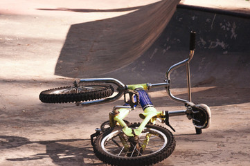 A bicycle lies near a hill descent in a skate park on a sunny day.