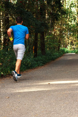 Young active handsome male healthy runner jogging outdoors along a scenic path in a forest. Vertical shot.