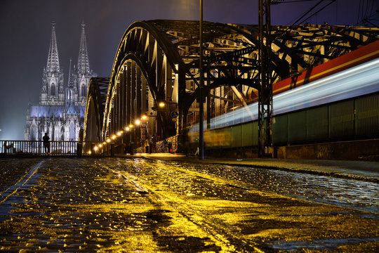 K&ouml;lner Dom Panorama mit Hohenzollernbr&uuml;cke aus Bodenh&ouml;he beim Regen und einem fahrendem Zug.