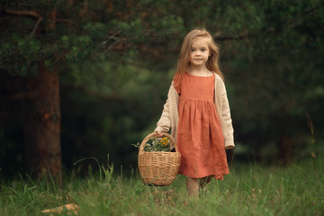 female kid holding wicker basket with flowers standing in the green forest, Full Length shot