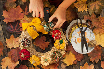 Female hands sew a textile pumpkin to decorate an autumn straw wreath on a wooden background. DIY...