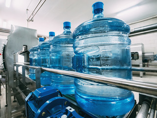 Blue plastic bottles with purified drinking water on automated conveyor production line. Water...