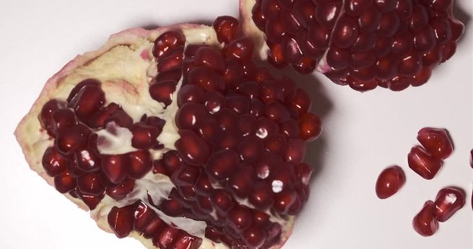 Pomegranate fruit and seeds, split open, rotating view from above on white background