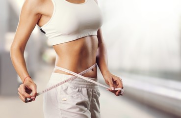 Weight loss, slim body, healthy lifestyle concept. Fit fitness girl measuring her waistline with measure tape on blue