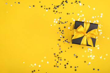 Gift box on yellow background with sparkling confetti.