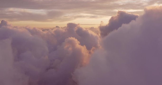 Aerial view flying above purple clouds at sunset with golden highlights