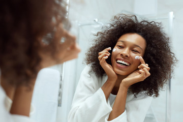 Skin care. Woman applying face cream looking in bathroom mirror
