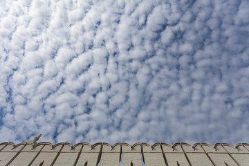The white stone wall of the monastery against a background of blue clouds covered with small clouds