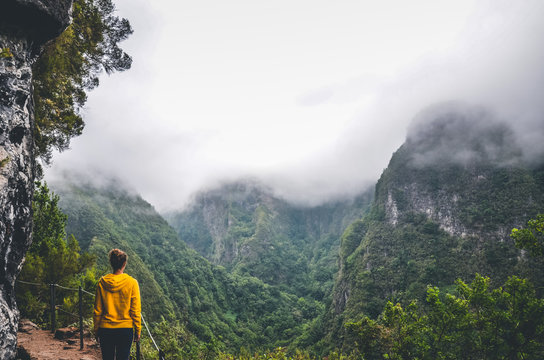 Young woman in yellow sweatshirt on a viewpoint in Levada Caldeirao Verde, Madeira, Portugal. Green scenic mountains in fog, misty landscape. Female traveler. Instagram, hipster filter