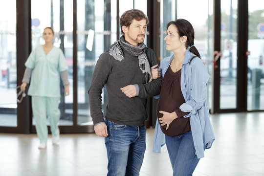 man helping heavily pregnant woman in hospital lobby - Powered by Adobe