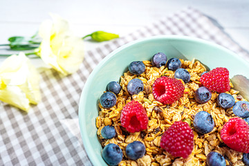 Bowl of homemade granola with fresh berries on gray wooden background.
