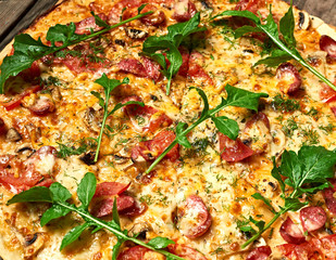 baked round pizza with smoked sausages, mushrooms, tomatoes, cheese and arugula leaves