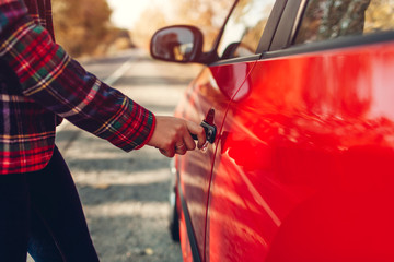 Opening car door. Woman opens red car with key on autumn road