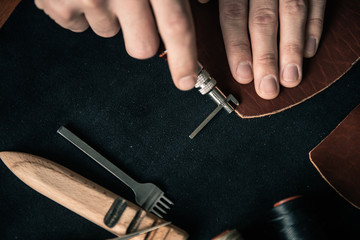a young tanner on a desktop in a workshop makes markings for punching seam holes on a piece of...