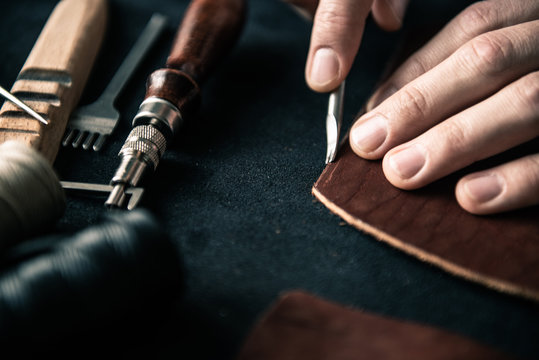 a young tanner on a desktop in a workshop chamfers a piece of brown leather with a special tool
