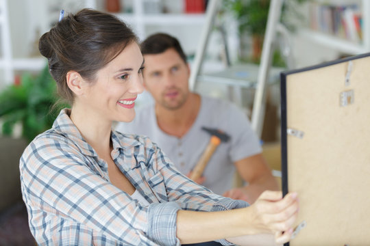 Positive Couple Hanging Art Picture In Their New Living Room