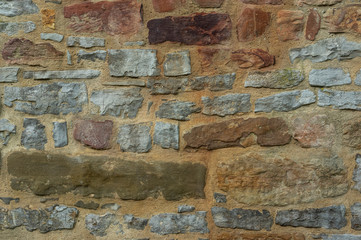 Natursteinmauer aus verschiedenen Natursteinen in verschiedenen Farben von dunkelgrau über gelb bis roten Sandstein