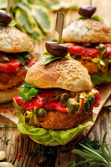 Pumpkin burgers with the addition of grilled peppers, fresh lettuce, herbs and capers on a wooden rustic background, close-up. Vegan burgers